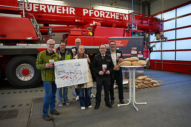 Der Leiter des Amt für Umweltschutz, Armin Aydt, Markus Schnepf, Sachgebietsleiter in der Abteilung Grünflächen- und Straßenmanagement des GTA, Frank Winterfeldt, stv. Sachgebietsleiter Katastrophenschutz/Einsatzvorbereitung der Feuerwehr Pforzheim sowie die Leiterin des Grünflächen- und Tiefbauamts (GTA), Sandra Heitkamp, Feuerwehrkommandant Sebastian Fischer und Bürgermeister Tobias Volle stehen vor einem Feuerwehrauto und präsentieren den Flyer der Feuerwehr zu Hochwasser- und Starkregenschutz.