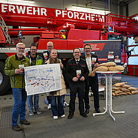 Der Leiter des Amt für Umweltschutz, Armin Aydt, Markus Schnepf, Sachgebietsleiter in der Abteilung Grünflächen- und Straßenmanagement des GTA, Frank Winterfeldt, stv. Sachgebietsleiter Katastrophenschutz/Einsatzvorbereitung der Feuerwehr Pforzheim sowie die Leiterin des Grünflächen- und Tiefbauamts (GTA), Sandra Heitkamp, Feuerwehrkommandant Sebastian Fischer und Bürgermeister Tobias Volle stehen vor einem Feuerwehrauto und präsentieren den Flyer der Feuerwehr zu Hochwasser- und Starkregenschutz.