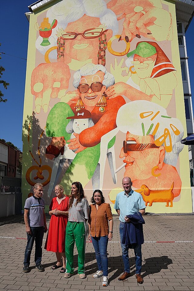 5 Personen vor einer mit gemalten Figuren verzierten Hauswand in der Kaiser-Friedrich-Straße
