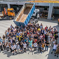 Circa 100 Teilnehmerinnen und Teilnehmer der Aktion Saubere Stadt jubeln für ein Bild vor einem Kipp-LKW, dessen Mulde die Müllmenge symbolisiert. 