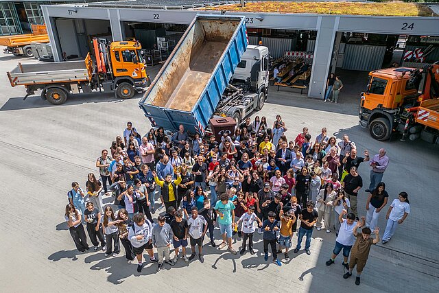 Circa 100 Teilnehmerinnen und Teilnehmer der Aktion Saubere Stadt jubeln für ein Bild vor einem Kipp-LKW, dessen Mulde die Müllmenge symbolisiert.