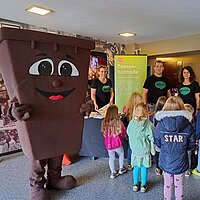 Eine Bio-Tonne als Maskottchen steht an einem Stand der Abfallwirtschaft. Davor stehen Kinder.