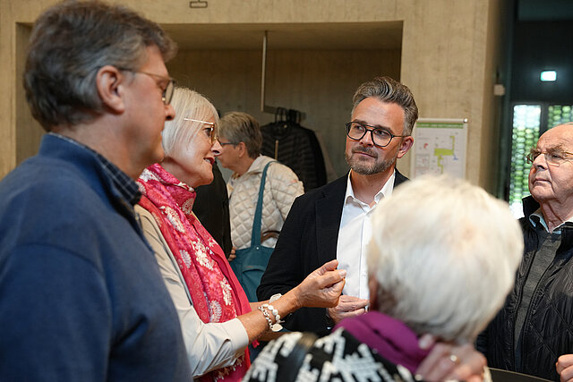 Eine Frau spricht ein einer Gruppe. Vier Personen um sie herum sehen sie an.