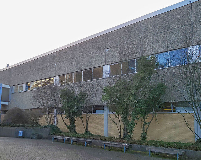 Eine Gebäudefassade mit Steinen, im Vordergrund sind einige Bäume zu sehen.