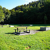 Mehrere Bank- und Tischkombinationen aus Holz und Feuerstellen aus Beton auf einer Wiese
