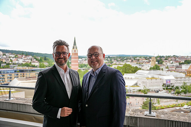 Auf dem Bild zu sehen sind der Oberbürgermeister der Stadt Pforzheim und der Intendant des Stadttheaters Pforzheim Markus Hertel auf dem Rathausbalkon vor dem Stadtpanorama mit dem Theater im Hintergrund