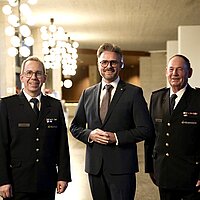 euerwehrkommandant Sebastian Fischer, Oberbürgermeister Peter Boch und Hubert Wollmer, Vorsitzender des Stadtfeuerwehrverbands Pforzheim stehen im Foyer des Rathauses und lächeln in die Kamera.
