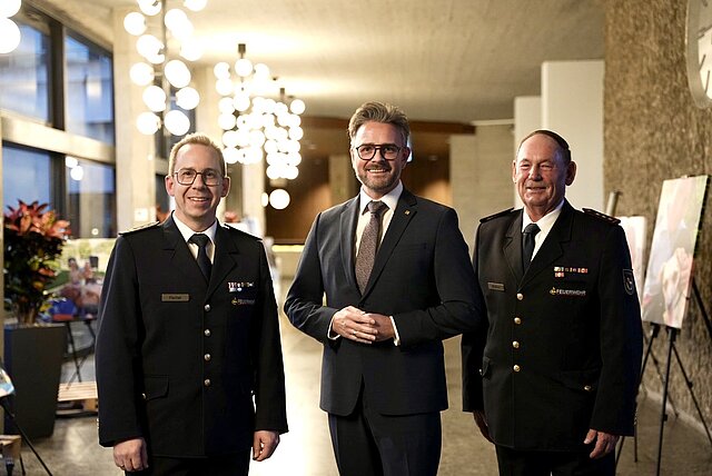 euerwehrkommandant Sebastian Fischer, Oberbürgermeister Peter Boch und Hubert Wollmer, Vorsitzender des Stadtfeuerwehrverbands Pforzheim stehen im Foyer des Rathauses und lächeln in die Kamera.