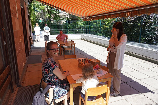 Erwachsene und ein Kind sitzen am Tisch mit Malsachen darauf - copyright:Stadt Pforzheim
