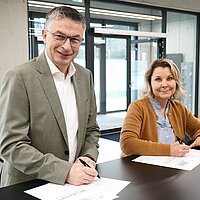 Ein Mann und eine Frau stehen an einem Tisch und unterschreiben ein Dokument