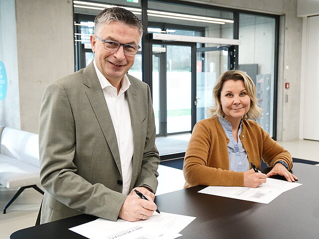 Ein Mann und eine Frau stehen an einem Tisch und unterschreiben ein Dokument