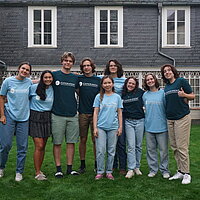 Farbfoto: 9 Schülerinnen und Schüler mit "Experiment"-T-Shirts auf einer Wiese vor einem Haus
