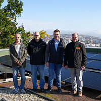 Auf dem Bild sind fünf Männer auf dem Dach des Reuchlin-Gymnasiums zu sehen, die sich über die Inbetriebnahme der dortigen Photovoltaikanlage freuen.
