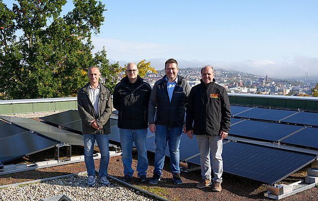 Auf dem Bild sind fünf Männer auf dem Dach des Reuchlin-Gymnasiums zu sehen, die sich über die Inbetriebnahme der dortigen Photovoltaikanlage freuen.