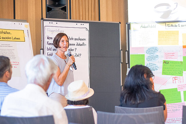 Person mit Mikrofon vor einer Tafel