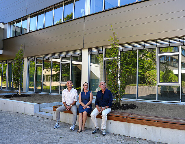 Drei Personen sitzen auf einer Bank vor der neuen Fassade der Heinrich-Wieland-Schule in Pforzheim