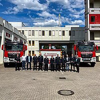 Farbfoto: Gruppenbild u. a. mit Feuerwehrkommandant Fischer  und Feuerwehr Fahrzeuge auf dem Gelände der Feuerwehr  