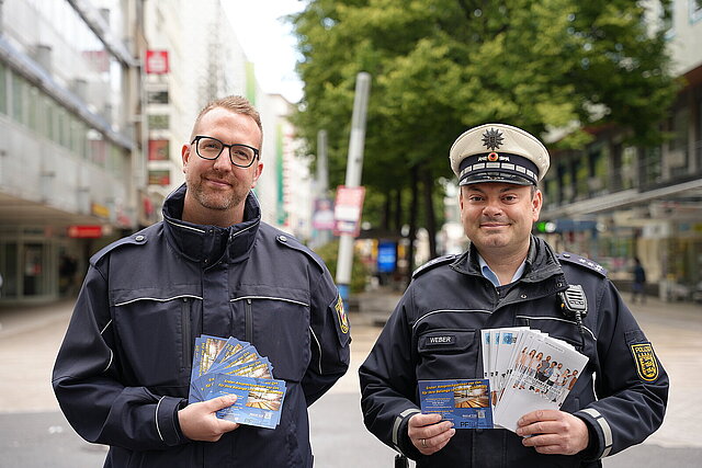 Farbfoto: zwei Polizeibeamte in der Innenstadt mit Flyern in der Hand