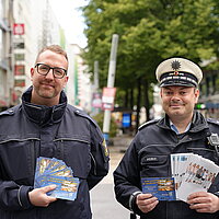 Farbfoto: zwei Polizeibeamte in der Innenstadt mit Flyern in der Hand
