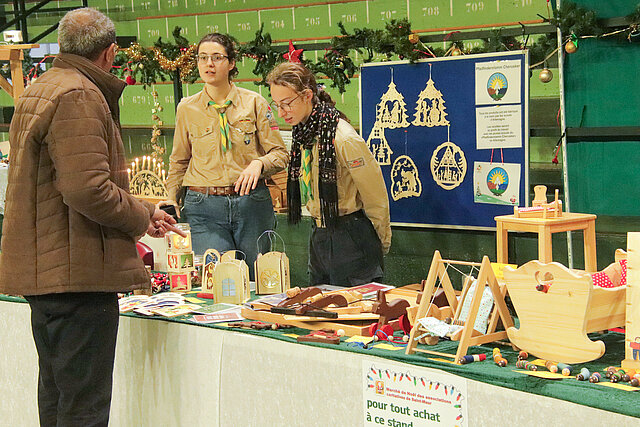 Zwei Frauen in Pfadfinderuniform hinter einem Stand auf einem Weihnachtsmarkt.