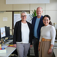 Drei Personen stehen neben einem Schreibtisch