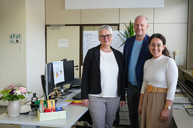Drei Personen stehen neben einem Schreibtisch