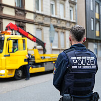 Ein Mann in Uniform von der Polizeibehörde steht vor einem gelben Laster