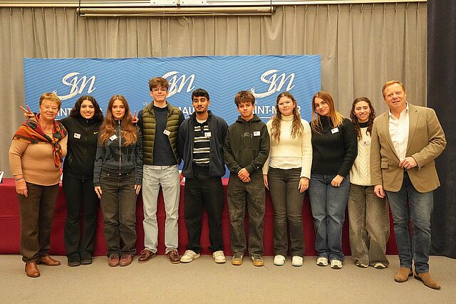 Eine Gruppe von Personen steht vor einem blauen und braunen Hintergrund.
