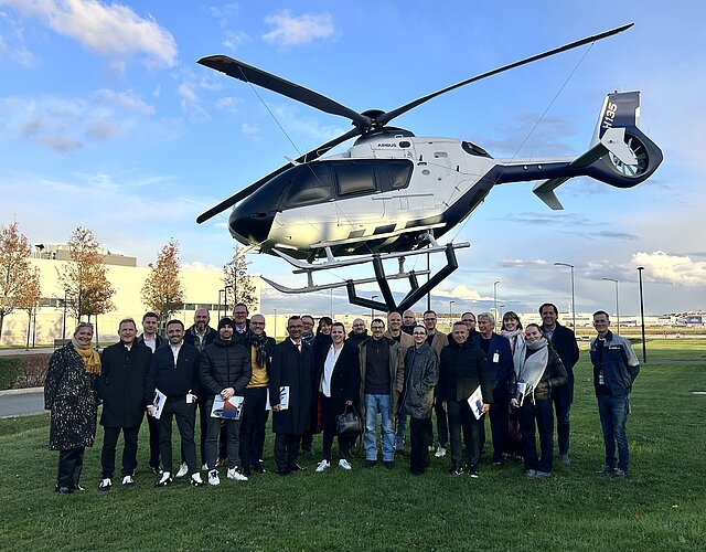 Eine Gruppe von Menschen steht vor einem in der Luft schwebenden Helikopter.