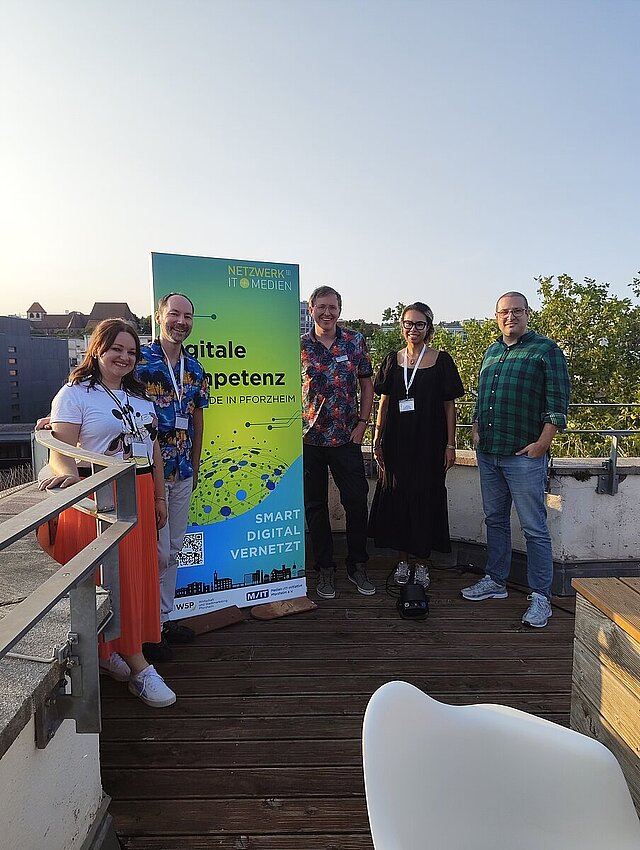 5 Personen auf einer Dachterrasse neben einem grünen Aufsteller.