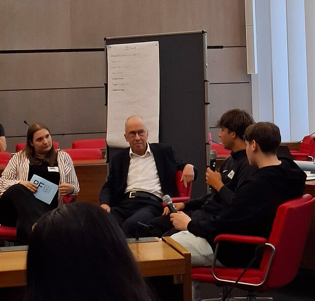 Auf dem Bild ist der Pforzheimer Bürgermeister Frank Fillbrunn zu sehen, wie er mit Schülern im Gespräch ist.