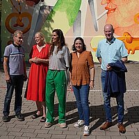 5 Personen vor einer mit gemalten Figuren verzierten Hauswand in der Kaiser-Friedrich-Straße