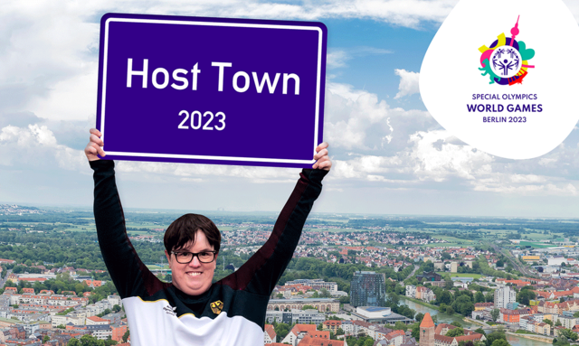 Foto: Sportlerin vom SOD hält Schild hoch mit der Aufschrift: Host Town 2023. Im Hintergrund eine Stadt - copyright:SOD
