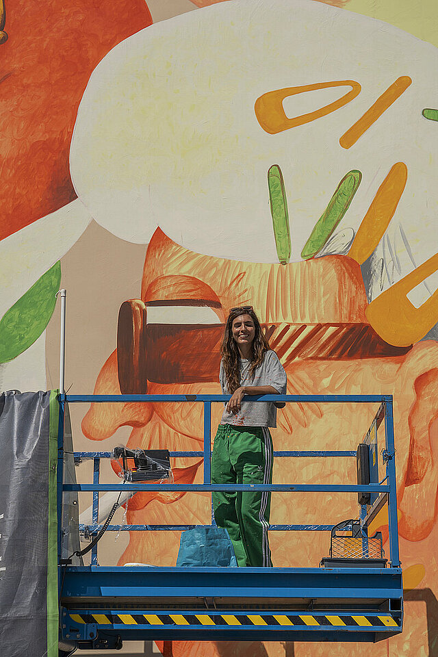 Die Künstlerin Marina CapdeVilla auf der Hebebühne vor ihrer gestalteten Fassade in der KF - copyright:Kulturamt Pforzheim / Jens Alemann