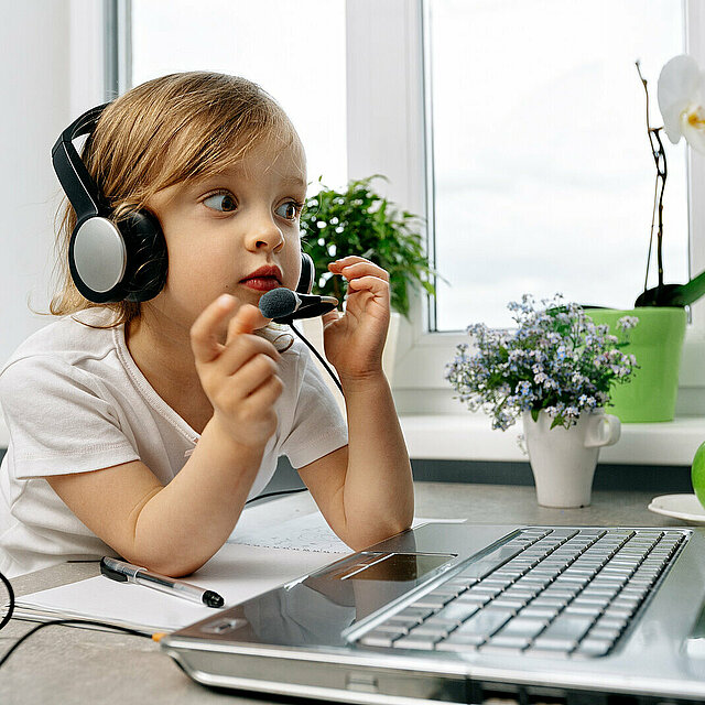 the child learns remotely, using a computer and headphones to listen to the lesson, an attentive student.