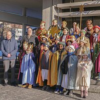 Viele Kinder mit Kronen und Umhängen stehen auf einer Treppe. 