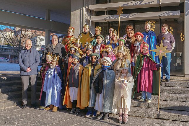 Viele Kinder mit Kronen und Umhängen stehen auf einer Treppe. 