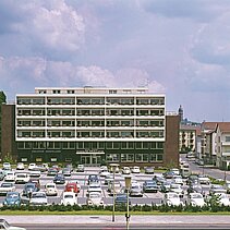 Farbfoto von 1974: Das Firmengebäude der Edelsteinschleiferei und Schmuckwarenfabrik Robert Schütt Witwe, Außenansicht mit Parkplatz. - copyright:Günter Beck