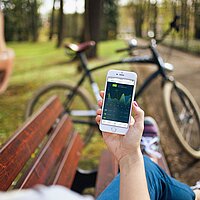 Frau hält Handy mit einer App auf dem Bildschirm in die Kamera. Im Hintergrund steht ein Fahrrad.