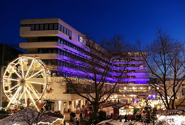 Auf dem Foto ist das Pforzheimer Rathaus zu sehen, das bei Dämmerung lila beleuchtet ist. Vor dem Rathaus auf dem Marktplatz ist der beleuchtete Weihnachtsmarkt zu sehen. Das Foto wurde von einer höheren Position aufgenommen. - copyright:Stadt Pforzheim