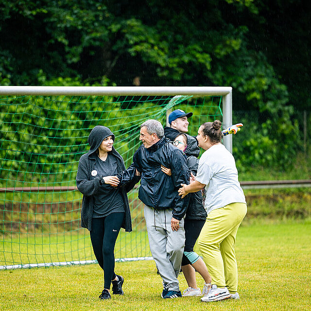 Drei Frauen Umarmen einen Mann auf dem Fußballfeld vor einem Tor. - copyright:Stadt Pforzheim