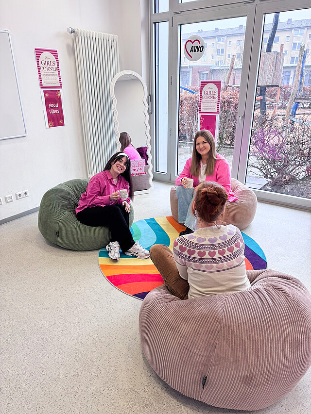 Drei Mädchen sitzen in einem Raum, der Girls Corner, auf Sitzsäcken und unterhalten sich.
