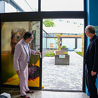 Zwei Männer im Anzug schauen durch eine offene Tür in einen neu gestalteten Innenhof. 