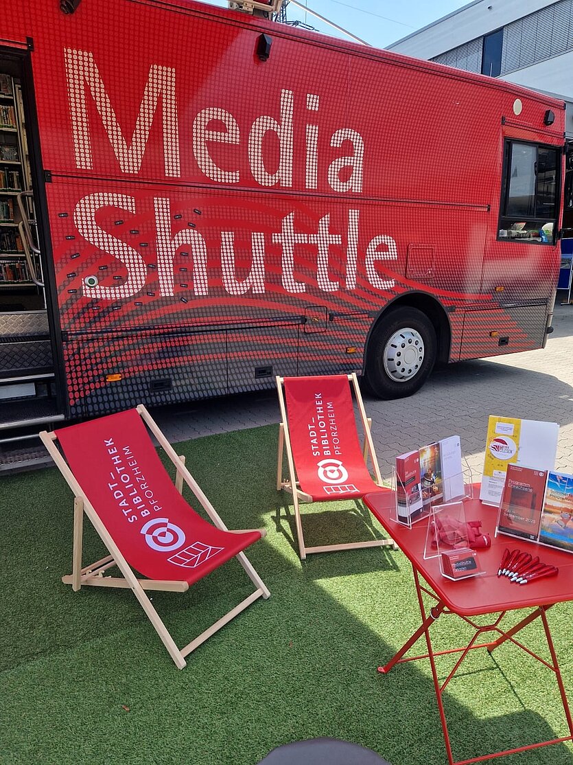Farbige Fotografie vom Bücherbus im Vordergrund Sonnenstühle und ein Tisch mit Flyern - copyright: Stadtbibliothek Pforzheim - Ersteller: Joachim Heiß