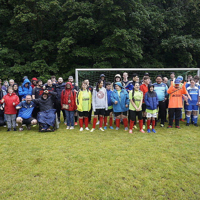 Ungefähr 40 Personen stehen im Regen auf einem Fußballfeld vor einem Tor und schauen in die Kamera - copyright:Stadt Pforzheim