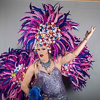 Eine Travestiekünstlerin im Pailettenkleid mit lila Federboa und Kopfschmuck.
