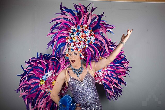 Eine Travestiekünstlerin im Pailettenkleid mit lila Federboa und Kopfschmuck.