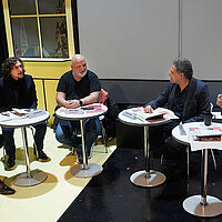 farbiges Gruppenbild: alle Personen sitzen an runden Tischen im Halbkreis