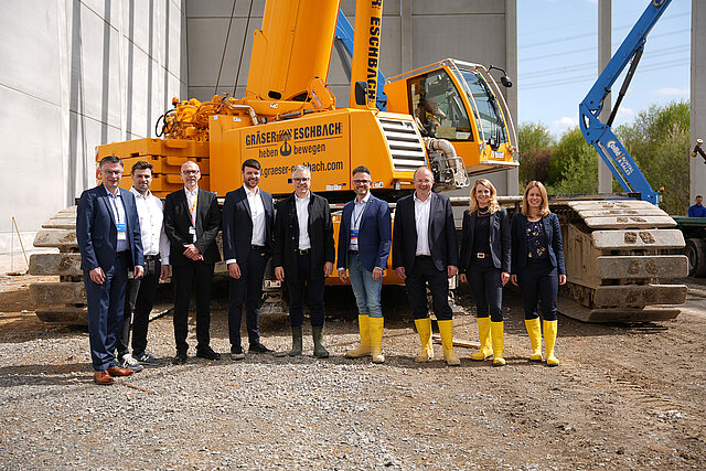 Farbfoto: Gruppenbild auf einer Baustelle vor einem orangefarbenen Kran 