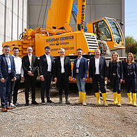 Farbfoto: Gruppenbild auf einer Baustelle vor einem orangefarbenen Kran 